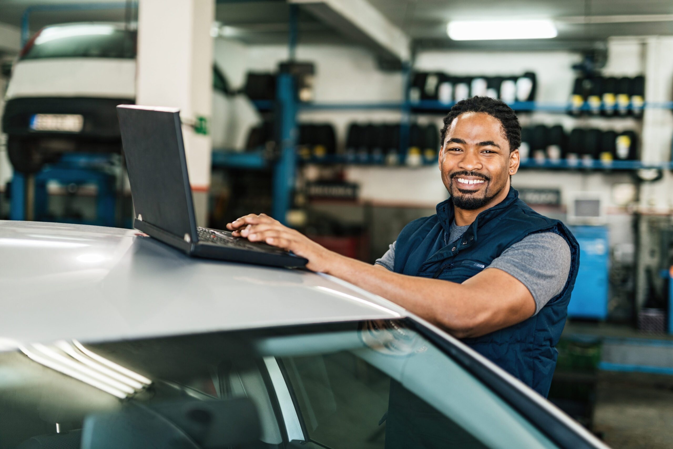 Happy African American car mechanic using laptop and looking at camera.