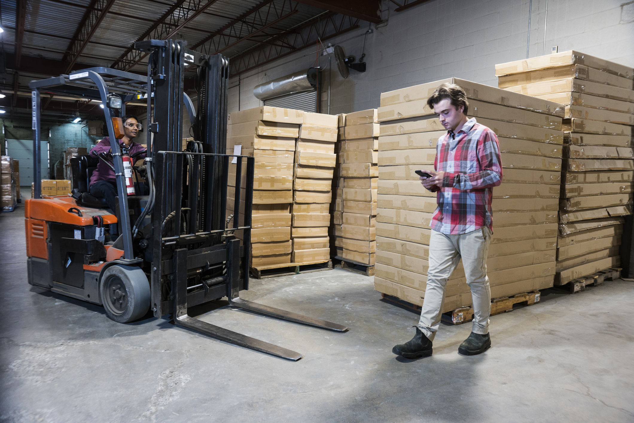 An accident waiting to happen.  An industrial worker using a cell phone in a warehouse.